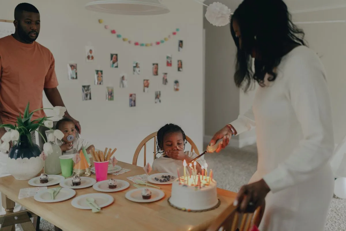 A family celebrates a child's birthday with cake and decorations in a cozy indoor setting.
