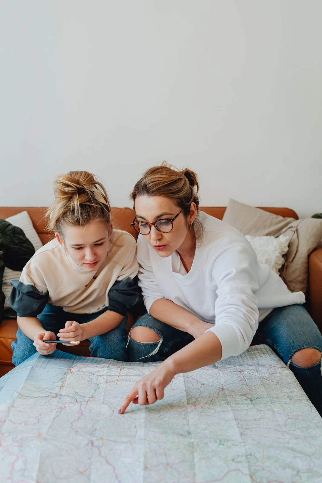 Mother and daughter planning a trip with map on the couch, casual setting.