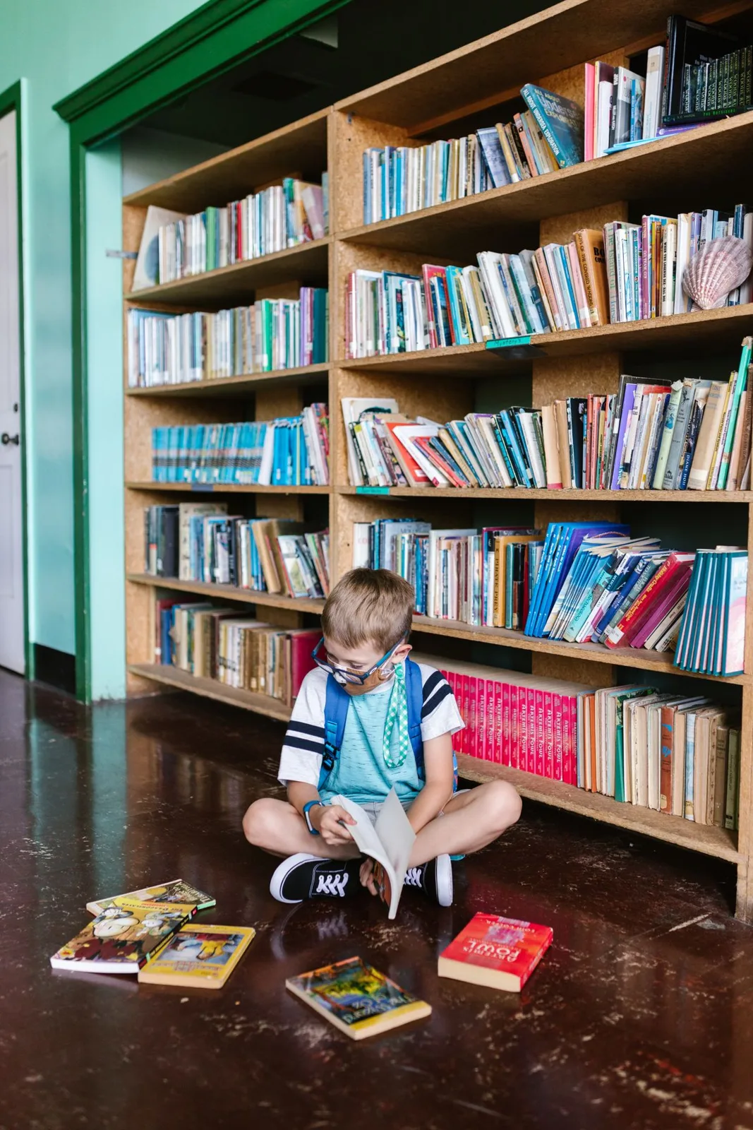 A child enjoys reading books inside a library, surrounded by shelves.