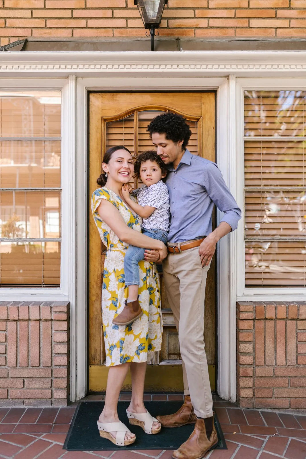 A joyful family portrait with parents and child in front of a house door.