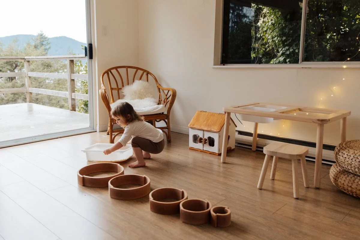 A young child enjoying playtime with wooden toys in a cozy, sunlit room with outdoor view.