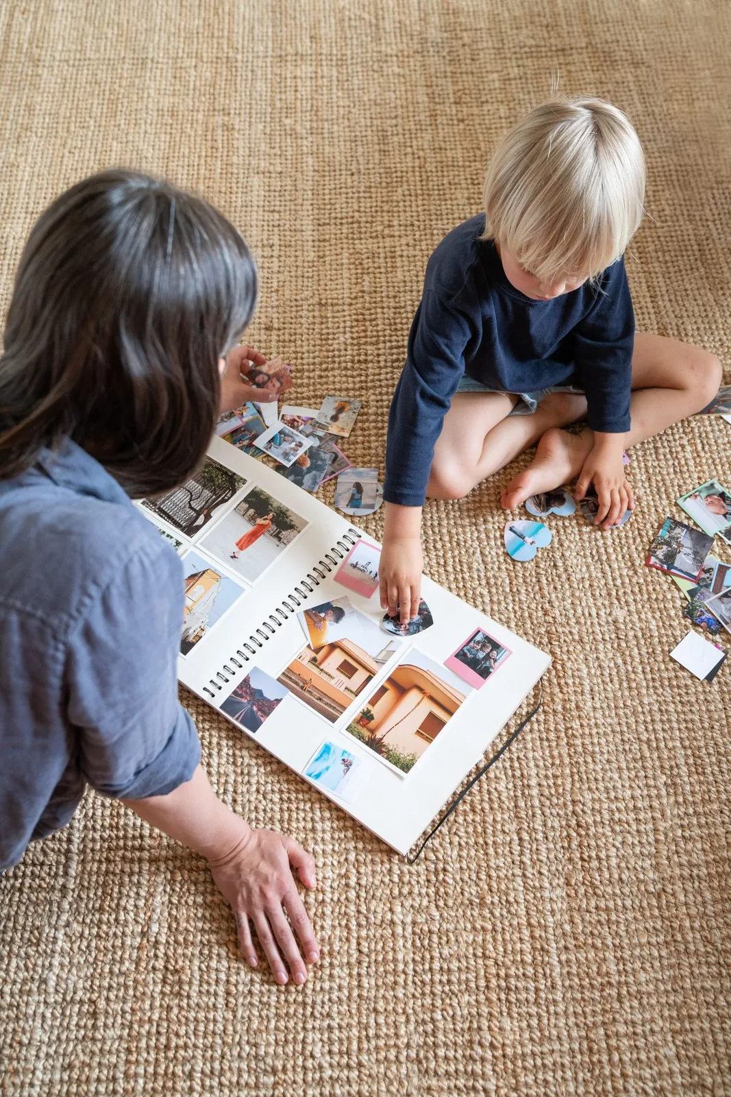 A woman and child engage in a creative scrapbook session on a carpeted floor.