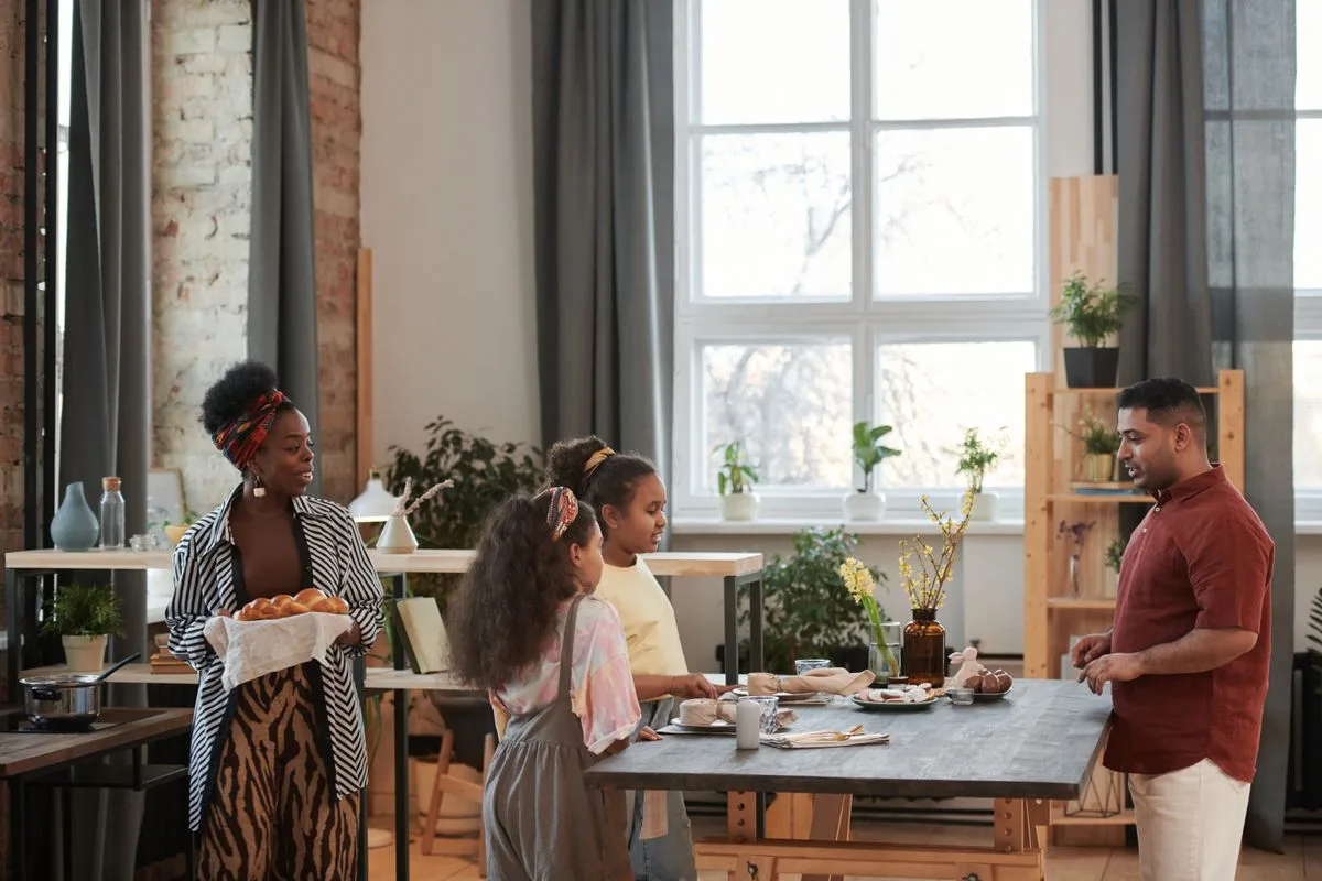 A family gathers around a table indoors, sharing breakfast and conversation.