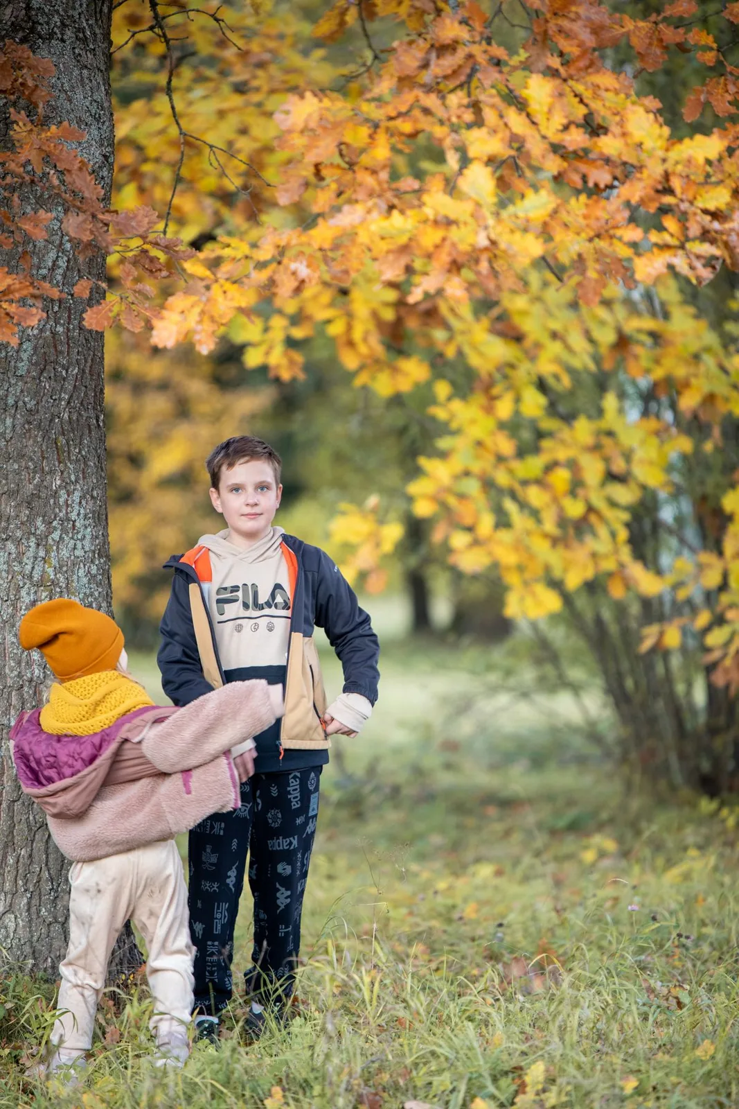 Two kids enjoying an autumn day under a vibrant tree with yellow leaves.