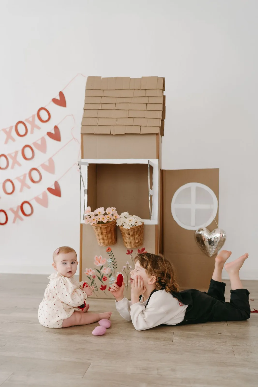Two children playing in a handmade cardboard house.