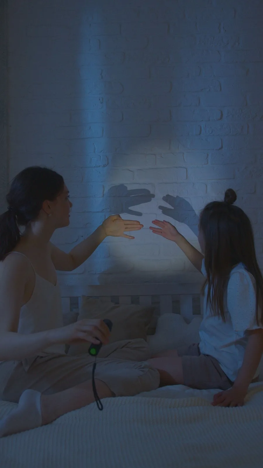 A tender moment as a mother and daughter create shadows with a flashlight in a cozy bedroom.