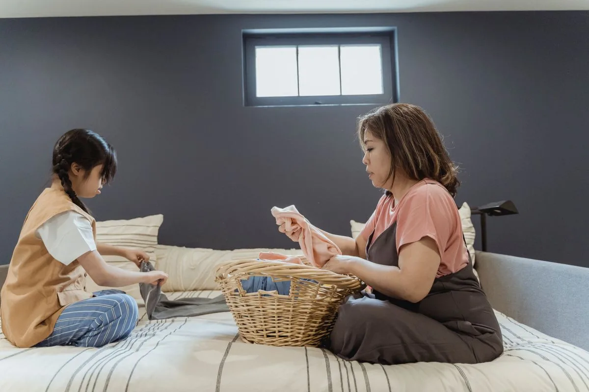 A mother and daughter engage in folding laundry on the bed.