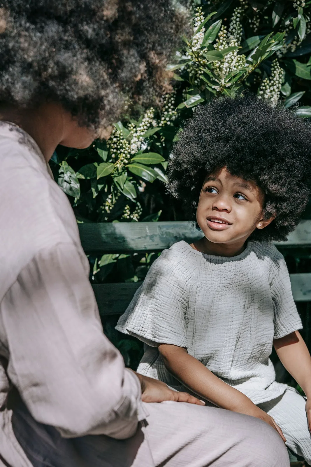 A mother and her child sitting on a bench, engaged in a thoughtful conversation in a sunny park.