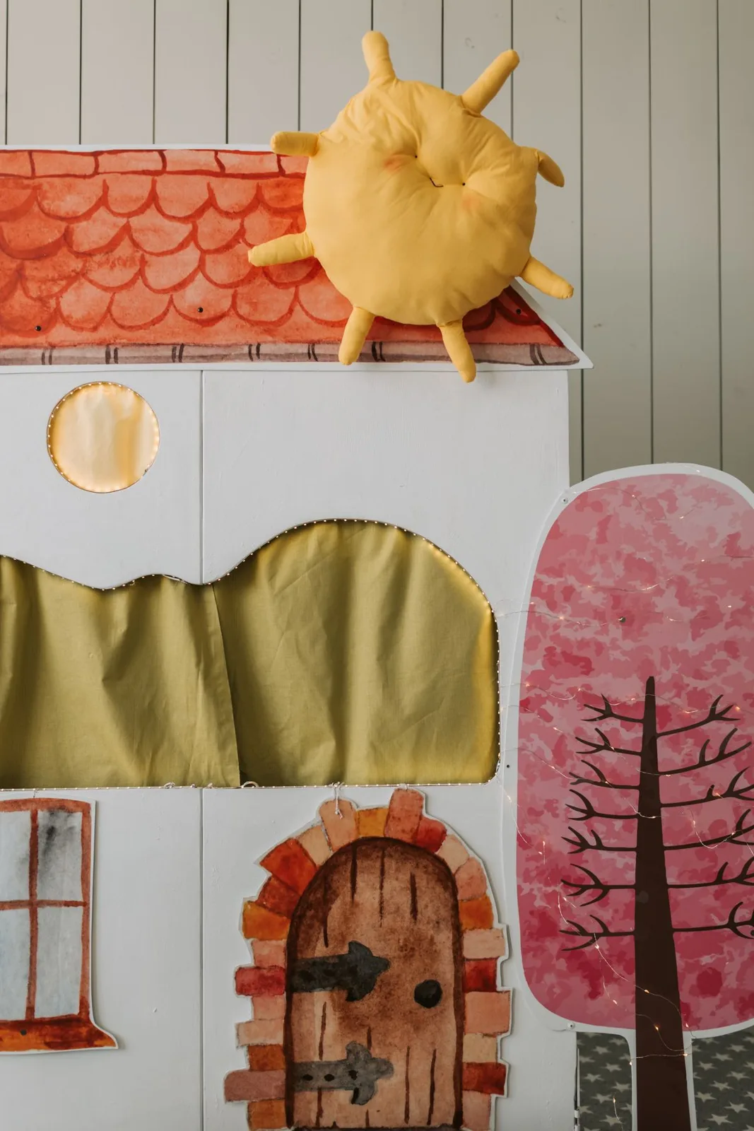 Vibrant puppet theater playhouse set with paper house, sun, and tree props for children's indoor play.