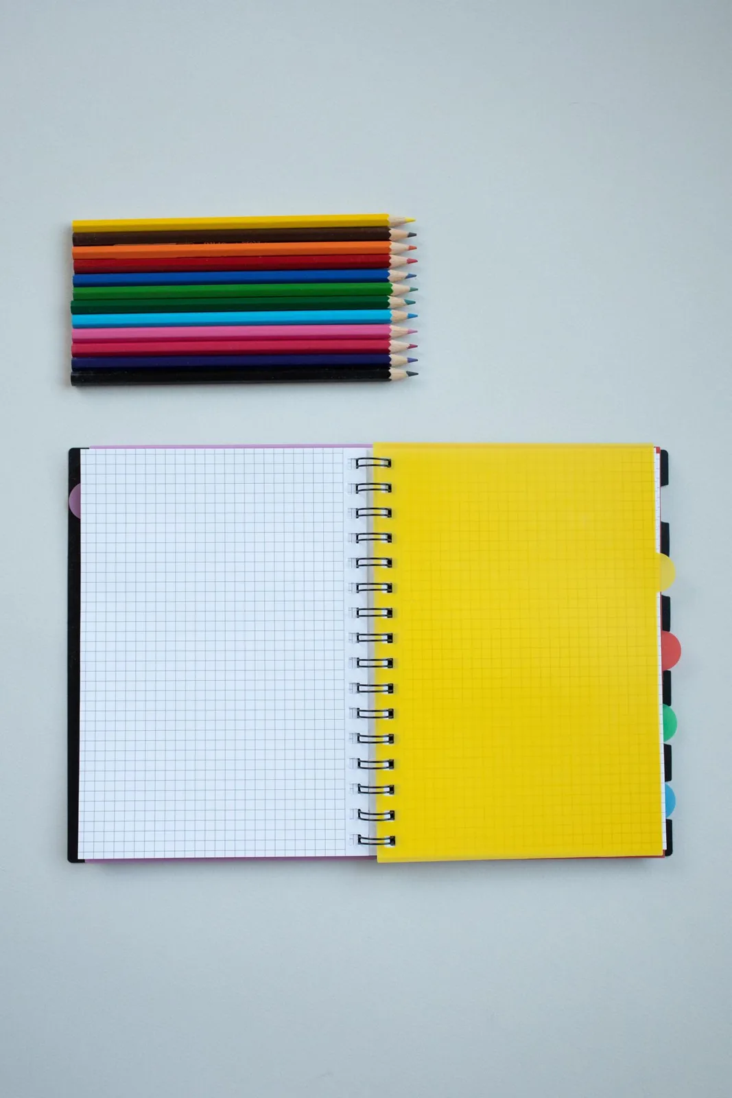 Colorful pencils and a spiral notebook on a white surface, ideal for back-to-school themes.