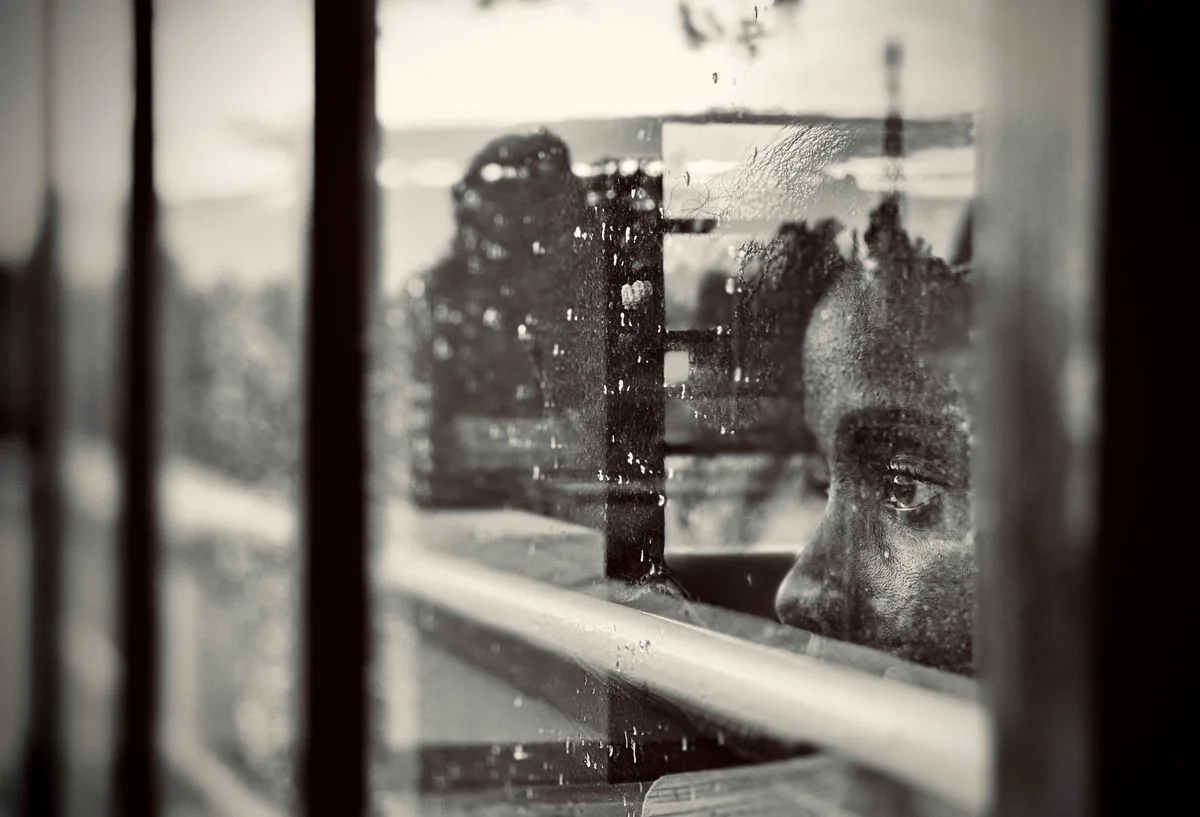 A child thoughtfully gazing through a rain-spattered window, lost in contemplation.