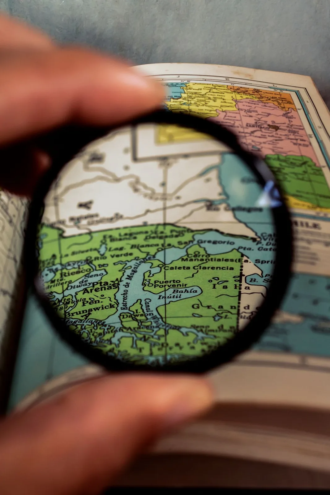 A hand holding a magnifying glass over a colourful map.