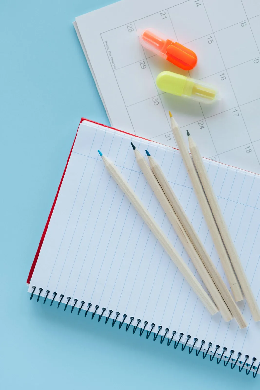 Aerial view of a notebook, calendar, and colored pencils on a blue background.