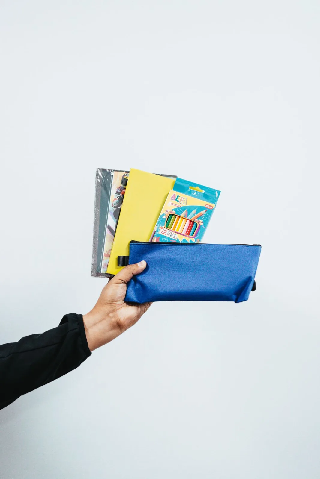 Hand holding colorful pencil case and school supplies on a plain background.