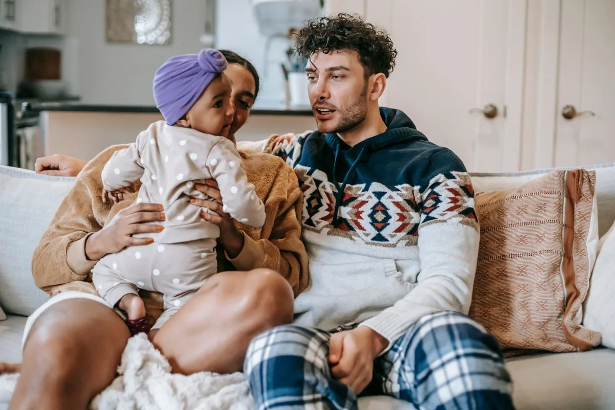Young multiethnic family with cute daughter talking on couch while spending weekend in living room