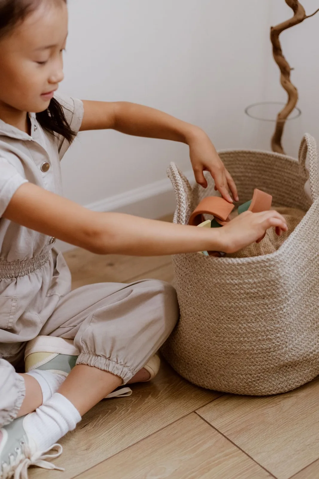 Young girl organizing toy blocks in a woven basket in a cozy indoor space.
